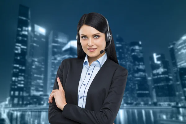 Portrait of brunette support phone operator with the headset. Business evening area of Singapore on the background. — Zdjęcie stockowe