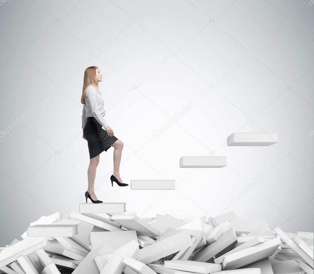 Young business woman is going up to the stairs. A concept of education process. White books on the floor.