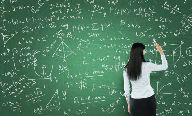 Rear view of a thoughtful woman who is writing math calculations on green chalk board.