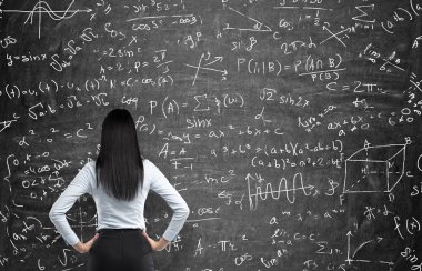 Rear view of a thoughtful woman who tries to solve math problems. Math calculations on black chalk board.