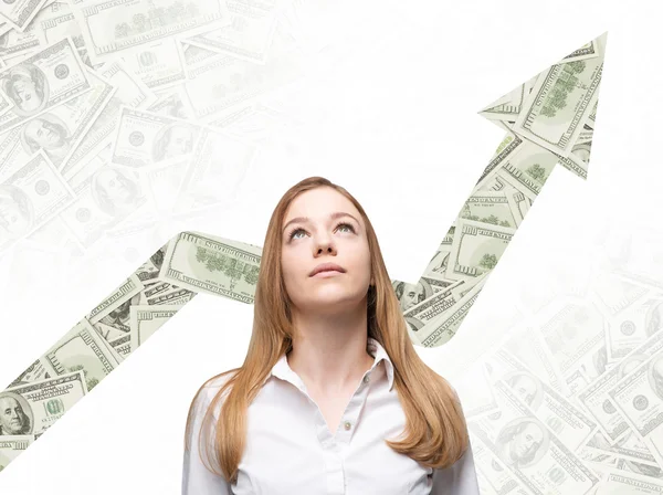 A business woman is looking up and thinking how to increase return of the business process. Increasing arrow which is made of dollar notes on the background. — Stock fotografie