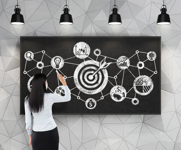 Wanita bisnis menggambar diagram alur target bisnis di papan tulis hitam. Ruang kontemporer dengan lampu pendent industri hitam . — Stok Foto