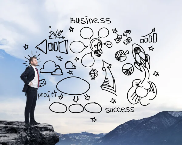 Businessman standing on a rock and looking at the flying business icons on the air. Mountain landscape. — Stok fotoğraf