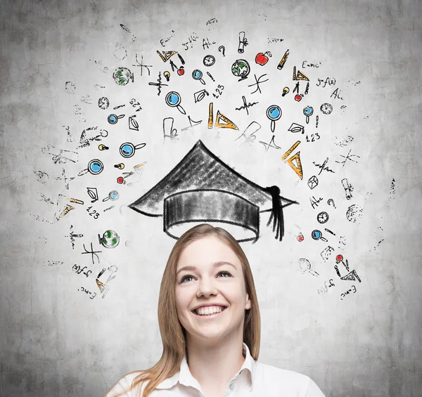 Young beautiful lady is thinking about studying at the university. Educational icons are drawn on the concrete wall. — Stock fotografie