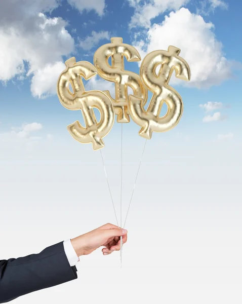 Una mano sostiene globos aéreos en forma de signos de oro en dólares. Cielo nublado fondo . — Foto de Stock