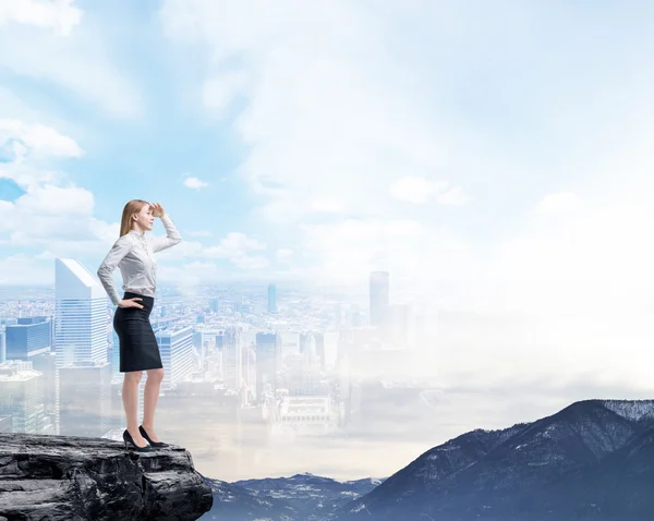 Business woman standing on a rock and looking at the flying business city. Illusion of the panoramic view of New York. — стокове фото