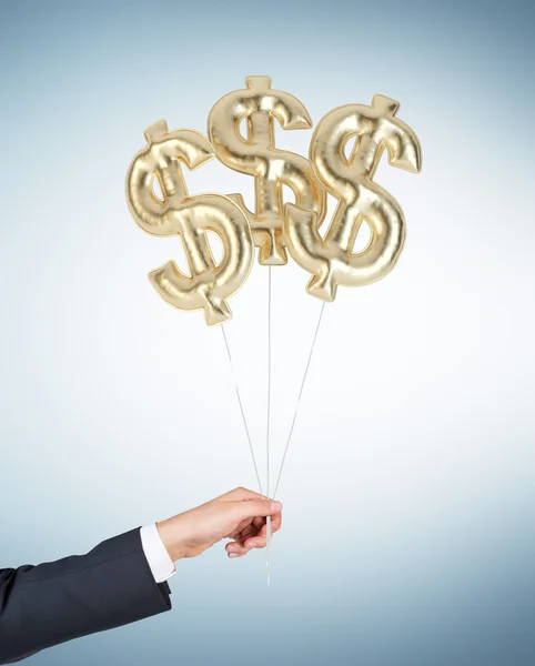 A hand is holding air balloons in a form of golden dollar signs. — Stock Photo, Image