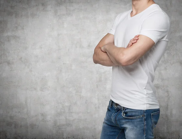 Side view of a person in a white V shape t-shirt with crossed hands. Concrete wall on background. — Stock Fotó