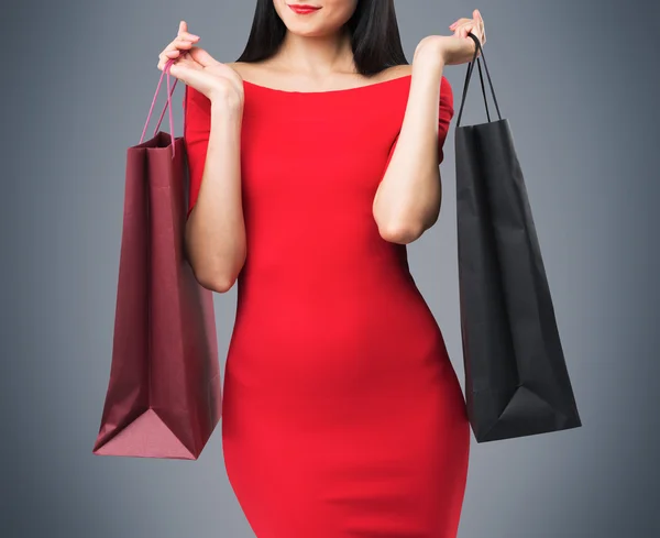 Hermosa mujer morena en un vestido rojo está sosteniendo bolsas de compras de lujo. Fondo gris . —  Fotos de Stock