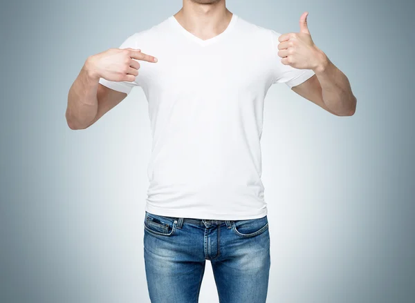 Close-up de um homem apontando o dedo para uma camiseta em branco, e o polegar para cima. Fundo azul . — Fotografia de Stock