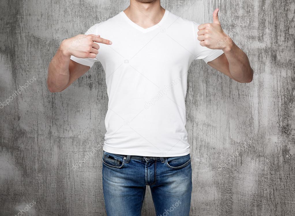 Close-up of a man pointing his finger to a blank t-shirt, and the thumb up. Concrete background.