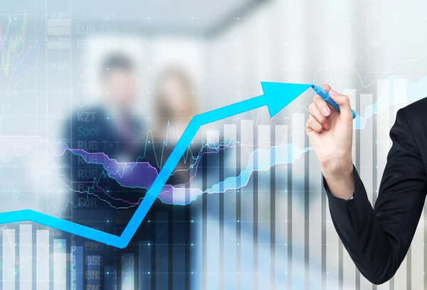 A hand is drawing a growing arrow on the glass scree, Blue dark background with financial graphs. Business couple in blur on the background. — Stock Photo, Image