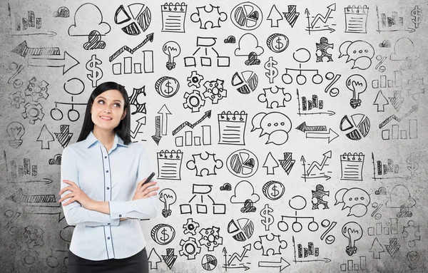 Young business woman is looking for the best solution for the business development process. Business icons are drawn over the concrete wall. — Stockfoto