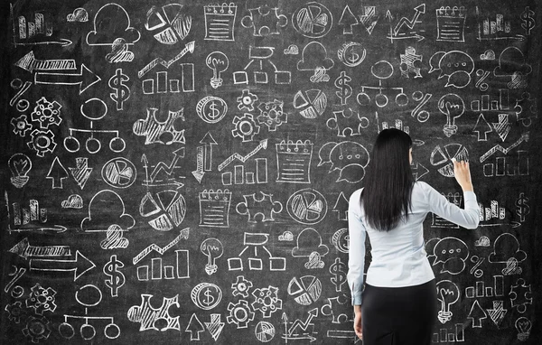 Vista trasera de la mujer de negocios que está dibujando iconos de negocios en la pizarra como una pared . — Foto de Stock