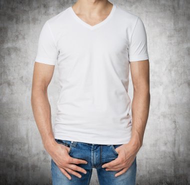 Young man in a white V shape t-shirt, hands in pockets. Concrete background.