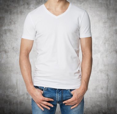 Young man in a white V shape t-shirt, hands in pockets. Concrete background. clipart