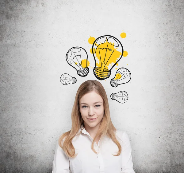 Charming young lady creates new business ideas. Drawn yellow light bulbs on the concrete wall. — Stock Photo, Image