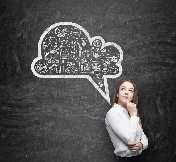 Side view of business lady, student, who is thinking about new business concepts. Drawn cloud with business icons on the black chalkboard. — Stock fotografie