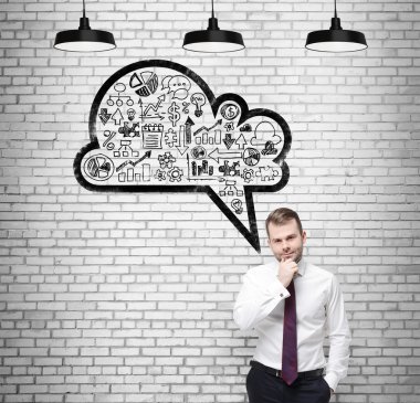 Front view of the confident businessman, student, who is thinking about new business concepts. Drawn cloud with business icons on the white brick wall.