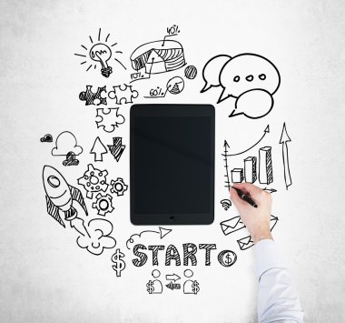 A tablet, digital device is surrounded by drawn business icons. A hand is drawing a bar chart. Concrete background.