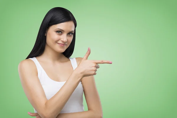 Brunette woman is in a white tank top. She points out something. Green background. — Φωτογραφία Αρχείου