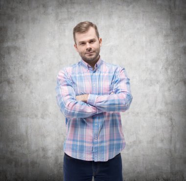Young handsome man in casual shirt with crossed hands. Concrete wall.