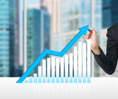 A hand is drawing a growing blue arrow as a concept of the success in business. Moscow cityscape in blur on the background.