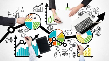 A top view of a brainstorm process. Business colleagues are analysing a business process. Laptop, tablet and legal pad on the table with drawn colourful charts which are drawn over the table.