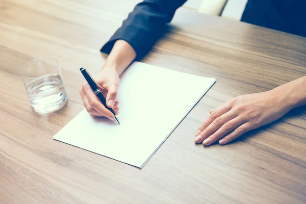 Nahaufnahme der Hände einer Geschäftsfrau, während sie einige wichtige Informationen aufschreibt. ein Glas Wasser, Papier und einen Stift. ein Konzept zur Ausarbeitung des Vertrages. Tonungsfilter. — Stockfoto