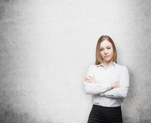 Young beautiful business lady with crossed hands. Concrete wall. — Stockfoto