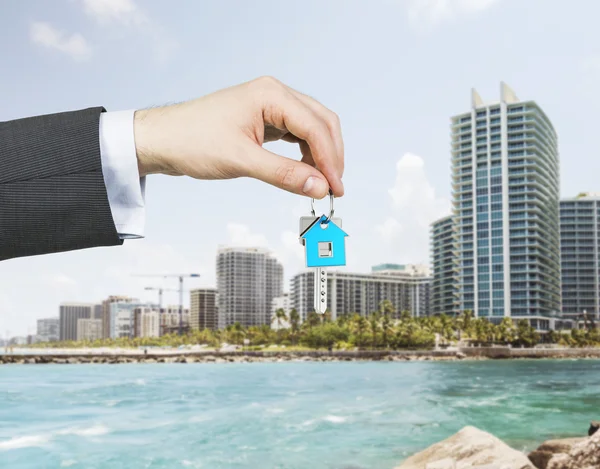 A hand is holding a key from the new home. A concept of real estate property agency. Miami cityscape on the background. — Stock Photo, Image