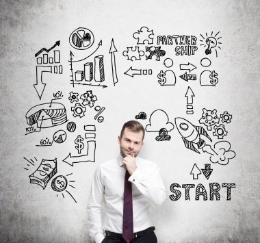 Confident businessman is thinking about business opportunities. A concept of brainstorm. Business icons are drawn behind the person on the concrete wall.