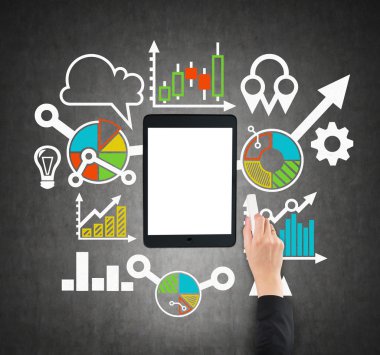A tablet, digital device with copy space screen is surrounded by drawn colourful business icons. A hand is drawing a flowchart. Black chalkboard.