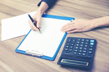 Closeup of a business woman's hands while writing down some essential quantitative information. Calculating machine, paper and a pen. Toning filter.