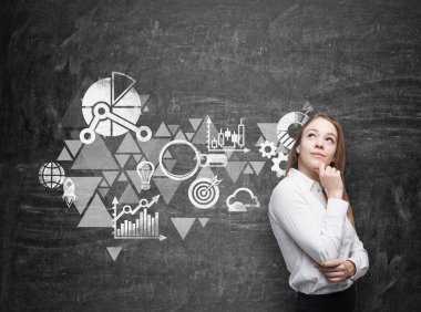 Young business woman is thinking about business optimisation scheme. Black chalk board as a wall on the background.