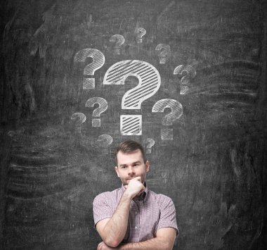 Brainstorming of young man. Question marks are drawn on the black chalkboard behind the person.