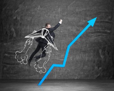 Businessman is taking of to the success with drawn wings. Rocketing blue arrow. Black chalkboard on the background.