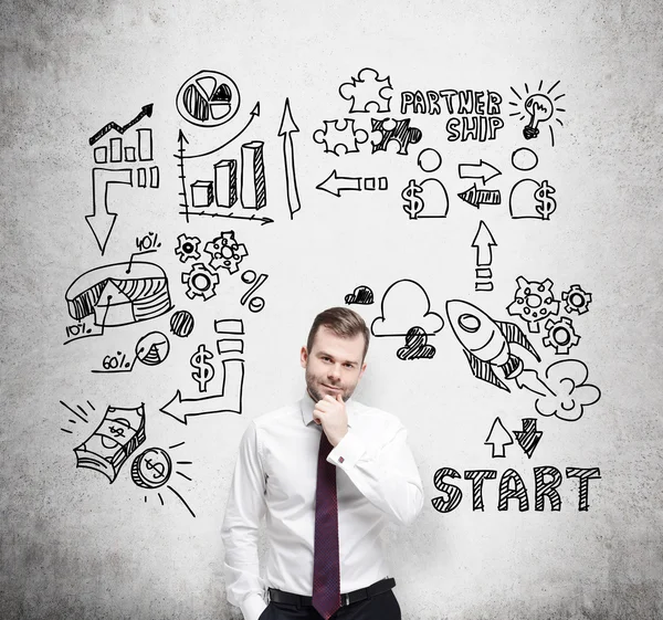 Confident businessman is thinking about business opportunities. A concept of brainstorm. Business icons are drawn behind the person on the concrete wall. — Stock fotografie