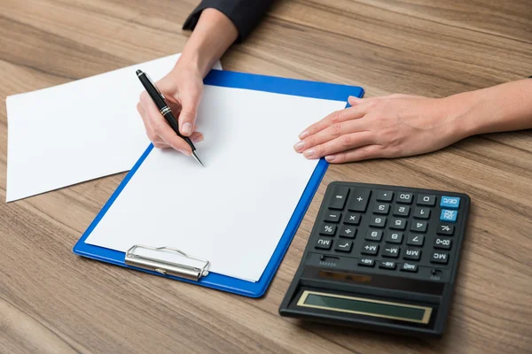 Fechar as mãos de uma mulher de negócios enquanto escreve algumas informações quantitativas essenciais. Máquina de calcular, papel e uma caneta. Filtro de afinação . — Fotografia de Stock