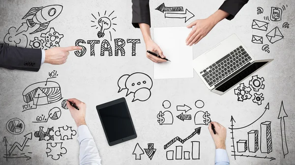 A top view of a brainstorm process. Business colleagues are build start up project. Laptop, tablet and legal pads on the table with drawn flowchart.