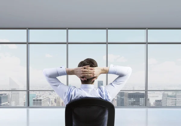 Rear view of the relaxing businessman is in a modern panoramic office. New York cityscape. — Stockfoto