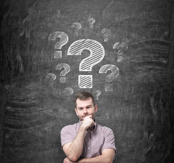 Brainstorming of young man. Question marks are drawn on the black chalkboard behind the person. — Stockfoto