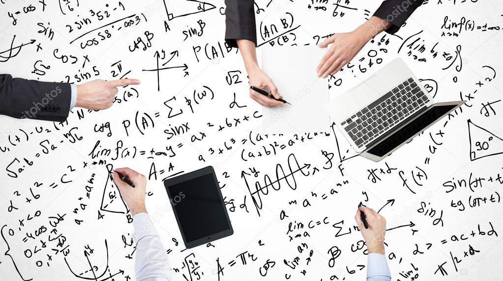 A top view of a brainstorm process. Colleagues are solving math problems. Laptop, tablet and math formulas are drawn over the surface on the table.