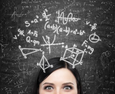 A forehead of the brunette lady and maths formulas are drawn on the black chalkboard.
