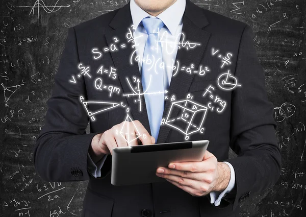 Young man in formal suit is holding a tablet with math formulas projection on the air. — ストック写真