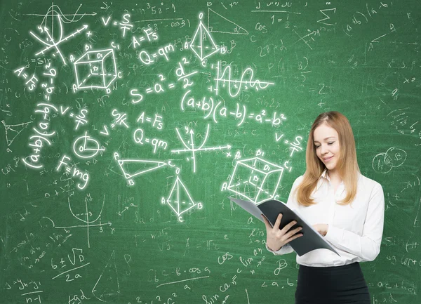 Junge Frau hält eine schwarze Aktenmappe in der Hand und auf der grünen Tafel sind verschiedene mathematische Formeln gezeichnet. — Stockfoto