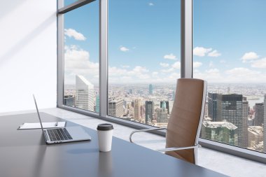 A workplace in a modern panoramic office with New York view. A grey table, brown leather chair. Laptop, writing pad for notes and a cap of coffee are on the table. Office interior. 3D rendering.