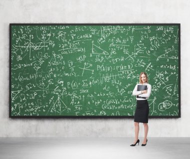 Full length of nice lady who holds black folder and stands in front of the green chalkboard, which is full of math formulas.