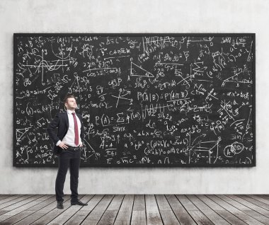 Side view of a confident young man who stands in front of black chalkboard which is full of math formulas. A concept of Analyst at investment bank.