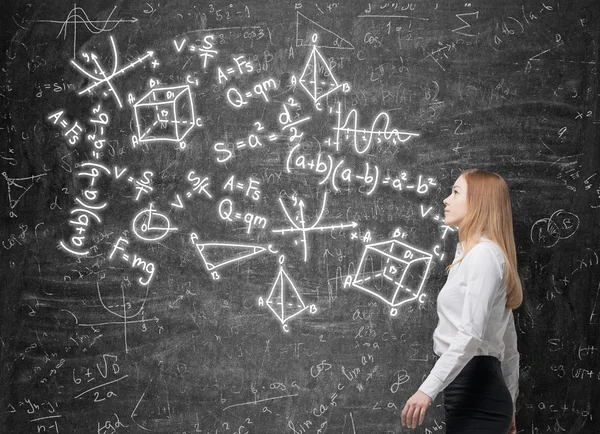 Junge Frau blickt auf die grüne Tafel mit mathematischen Formeln. — Stockfoto